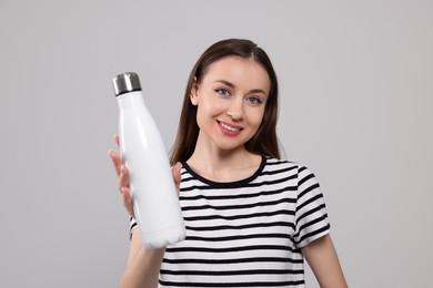 Beautiful young woman with thermos bottle on light grey background