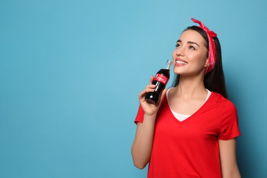 Photo of MYKOLAIV, UKRAINE - JANUARY 27, 2021: Young woman drinking Coca-Cola on light blue background. Space for text