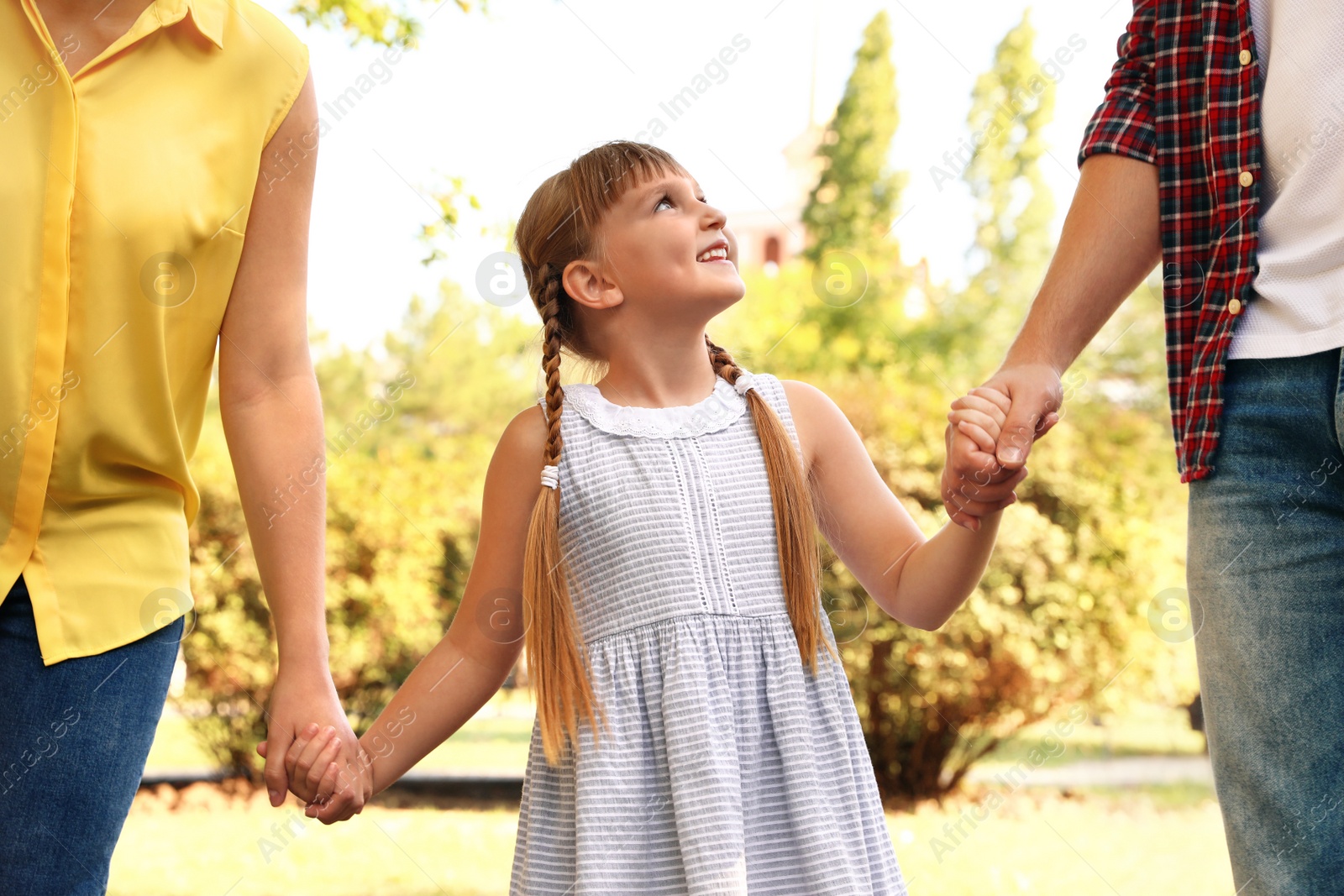 Photo of Little girl and her parents holding hands outdoors. Family weekend