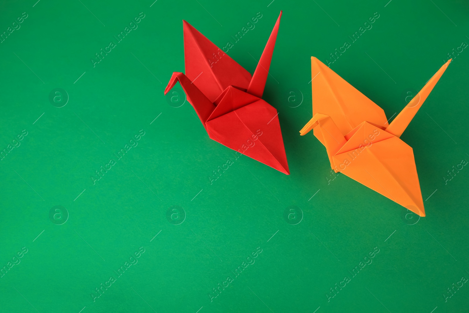 Photo of Colorful paper origami cranes on green background, above view. Space for text