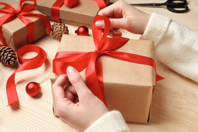 Photo of Christmas present. Woman tying ribbon bow on gift box at wooden table, closeup