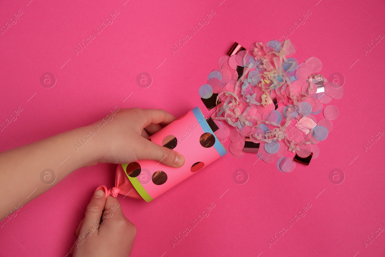 Photo of Woman holding party popper with serpentine and confetti on pink background, top view