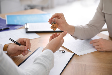 Photo of Real estate agent giving key with trinket to client in office, closeup