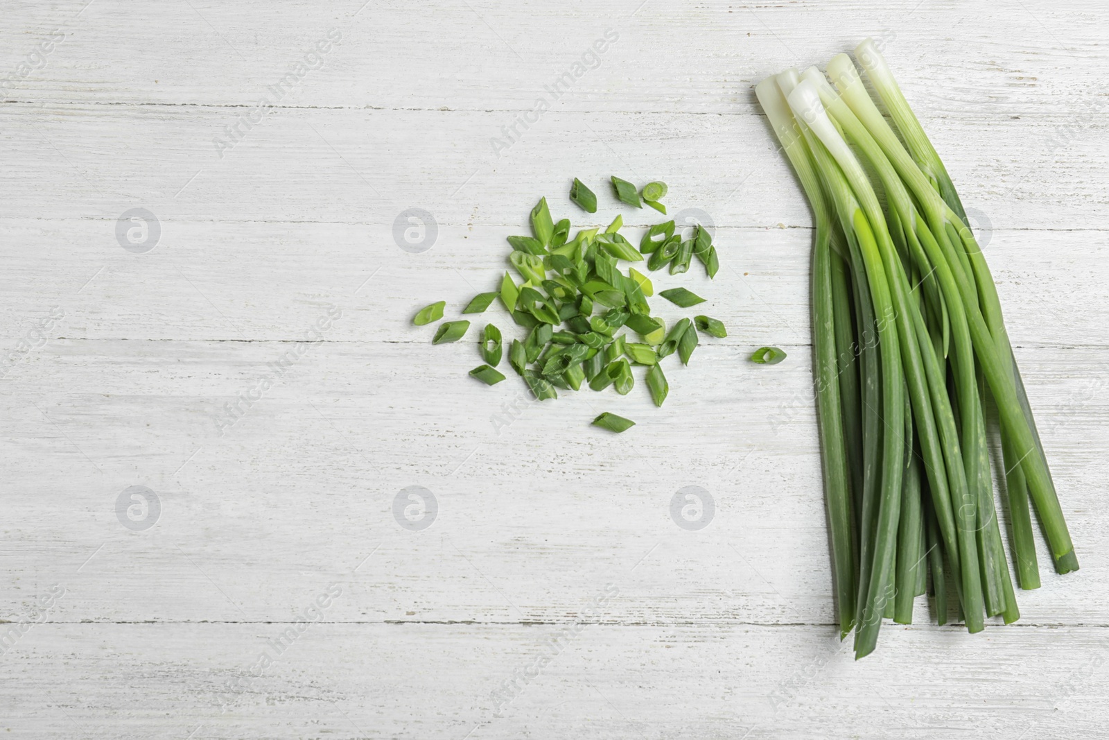 Photo of Cut and fresh green onions on white wooden table, flat lay with space for text