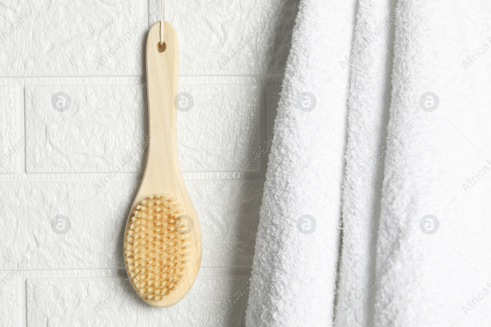 Photo of Bath accessories. Bamboo brush and terry towel on white brick wall