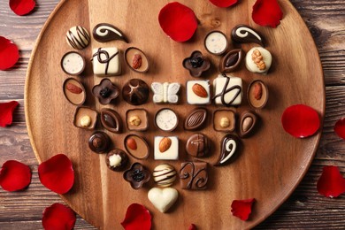 Heart made with delicious chocolate candies and rose petals on wooden table, top view