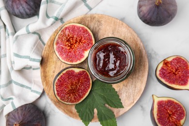 Glass jar of tasty sweet fig jam and fruits on white marble table, flat lay