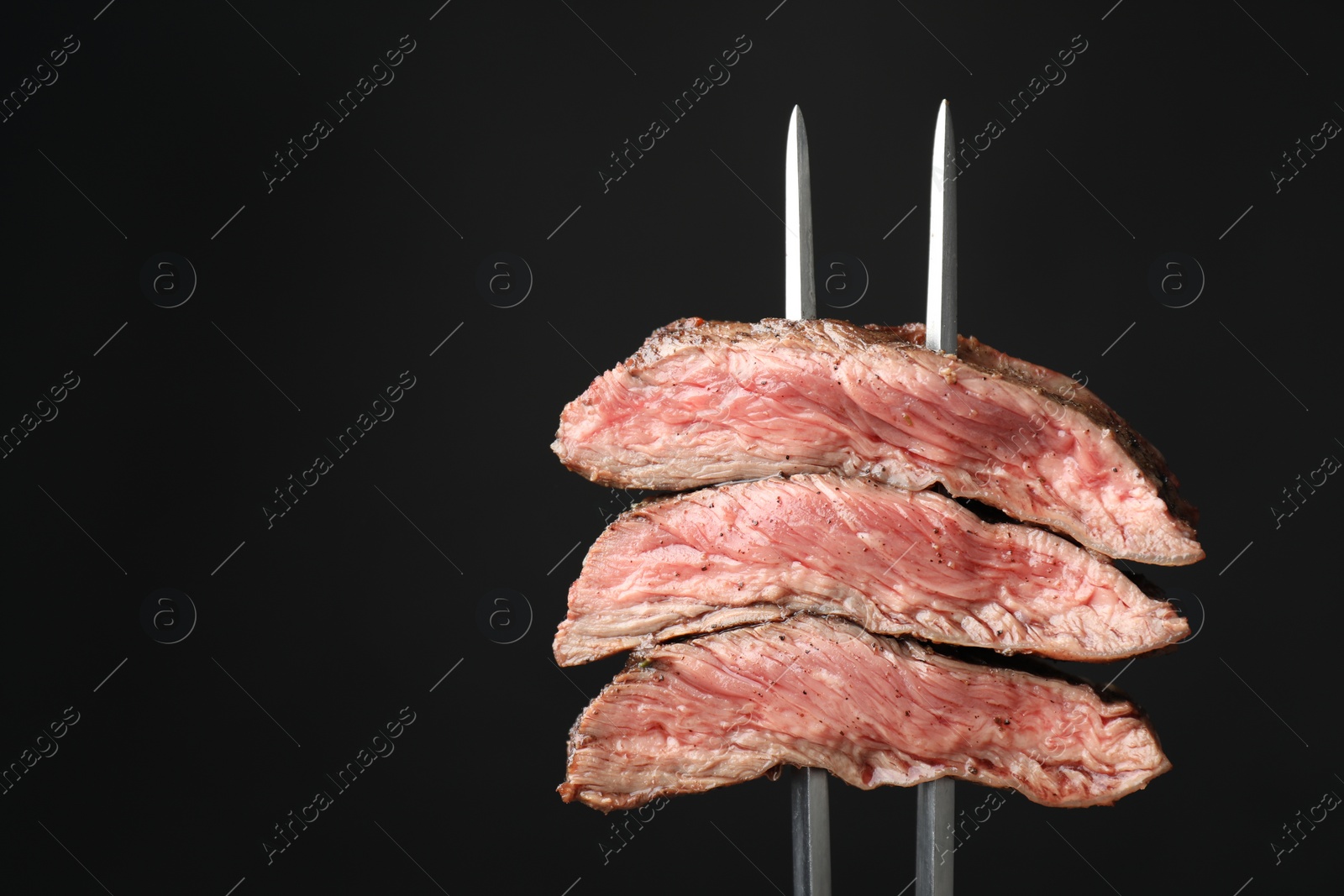 Photo of Meat fork with grilled beef pieces on black background, closeup. Space for text