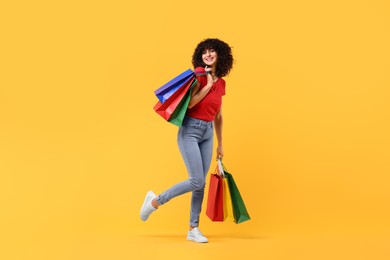 Happy young woman with shopping bags on yellow background