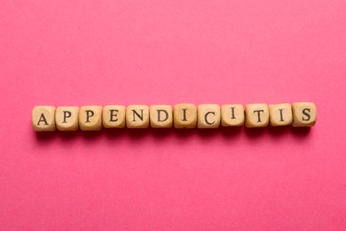Photo of Word Appendicitis made of wooden cubes with letters on pink background, top view