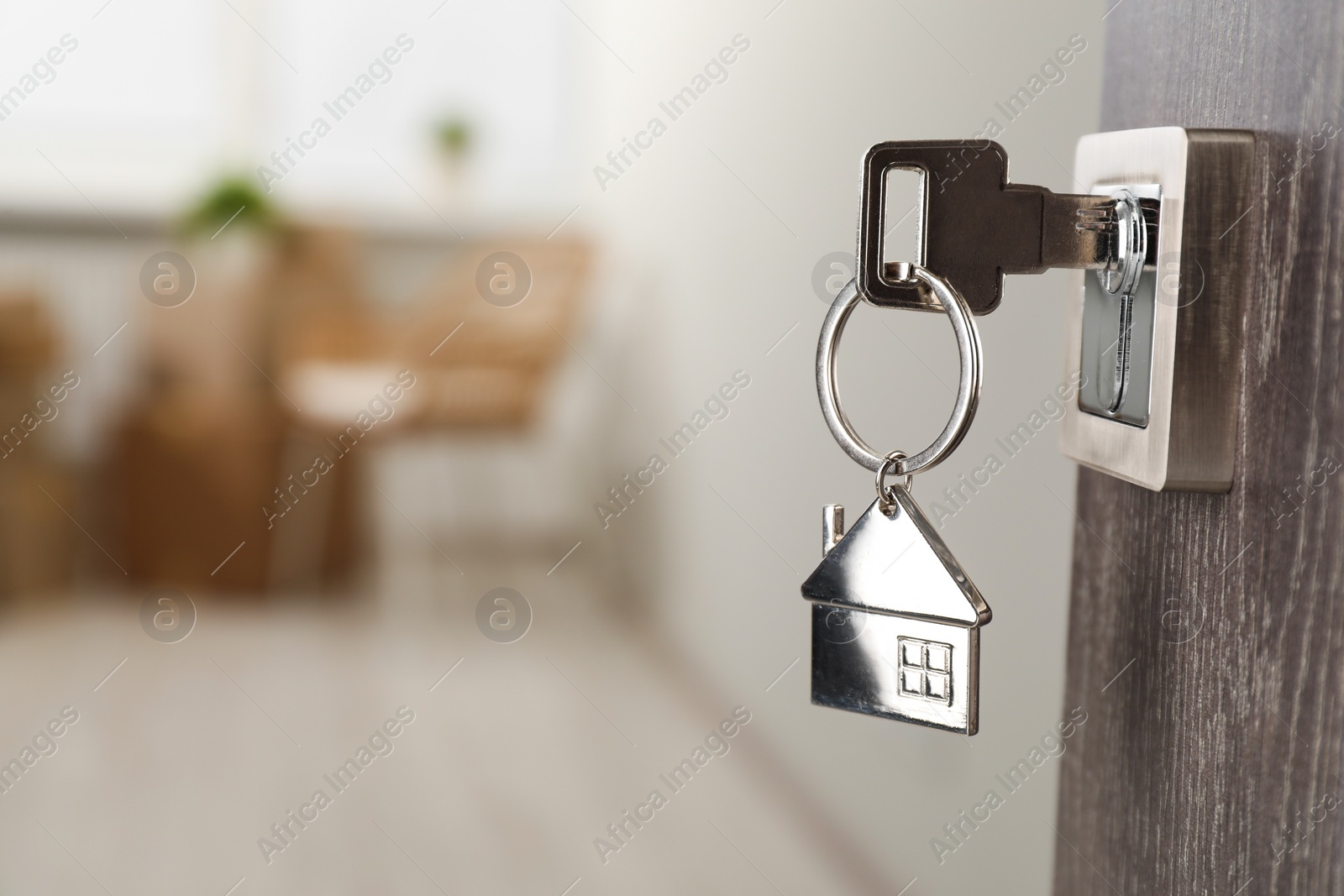 Photo of Mortgage and real estate. Open door with key and house shaped keychain against blurred background, space for text