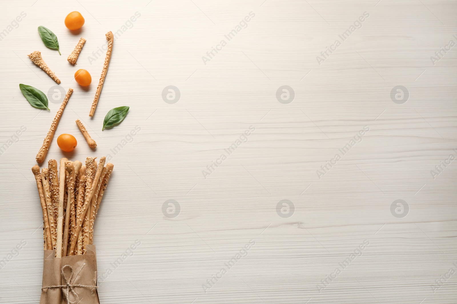 Photo of Delicious grissini sticks, basil leaves and yellow tomatoes on white wooden table, flat lay. Space for text