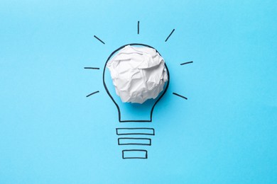 Photo of Idea concept. Light bulb made with crumpled paper and drawing on light blue background, top view