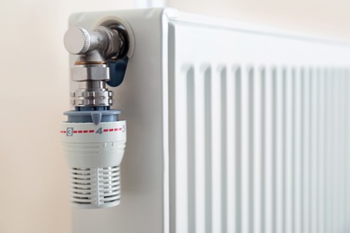Photo of Heating radiator with thermostat near light wall, closeup