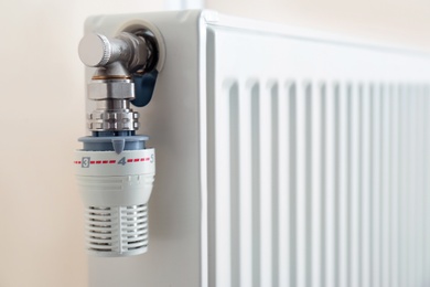 Heating radiator with thermostat near light wall, closeup