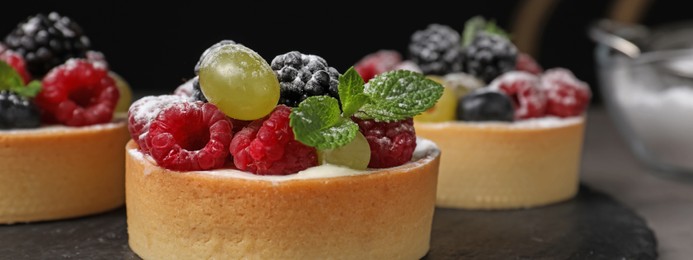 Image of Delicious tartlets with fresh berries on slate board, closeup. Banner design