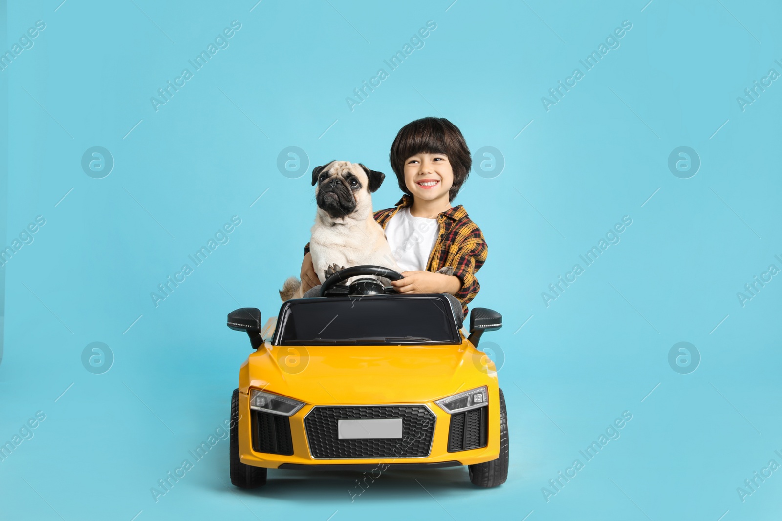 Photo of Little boy with his dog in toy car on light blue background