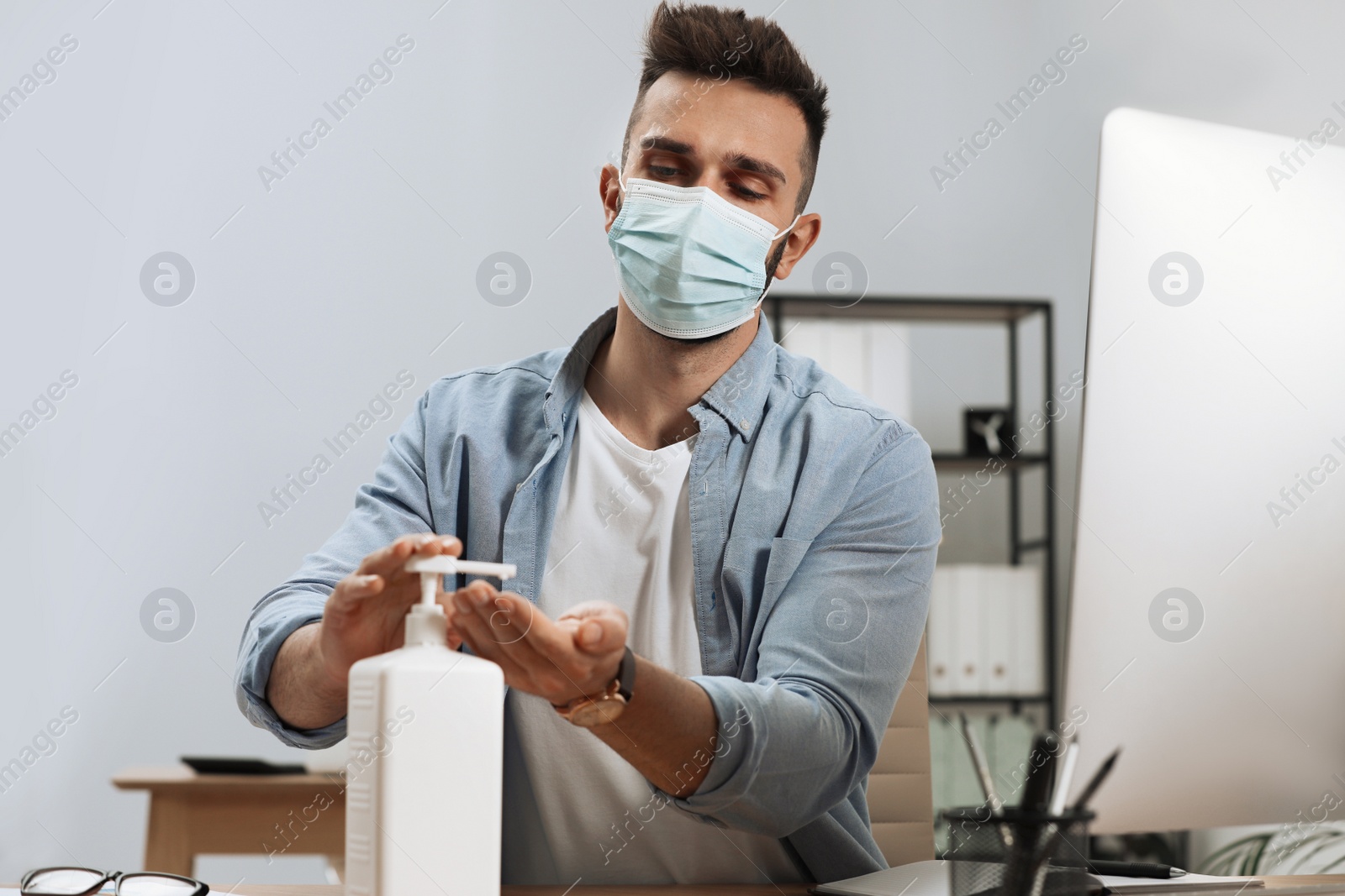 Photo of Man applying hand sanitizer at workplace in office. Personal hygiene during Coronavirus pandemic