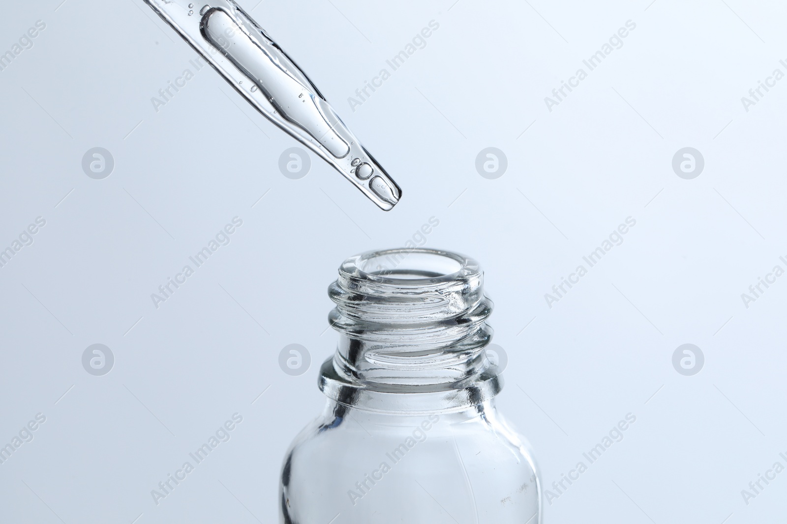 Photo of Dripping liquid from pipette into glass bottle on light blue background, closeup