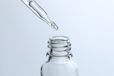 Dripping liquid from pipette into glass bottle on light blue background, closeup