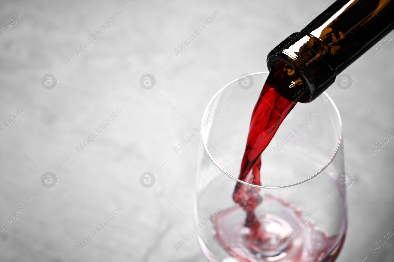 Photo of Pouring red wine from bottle into glass on light background, closeup. Space for text