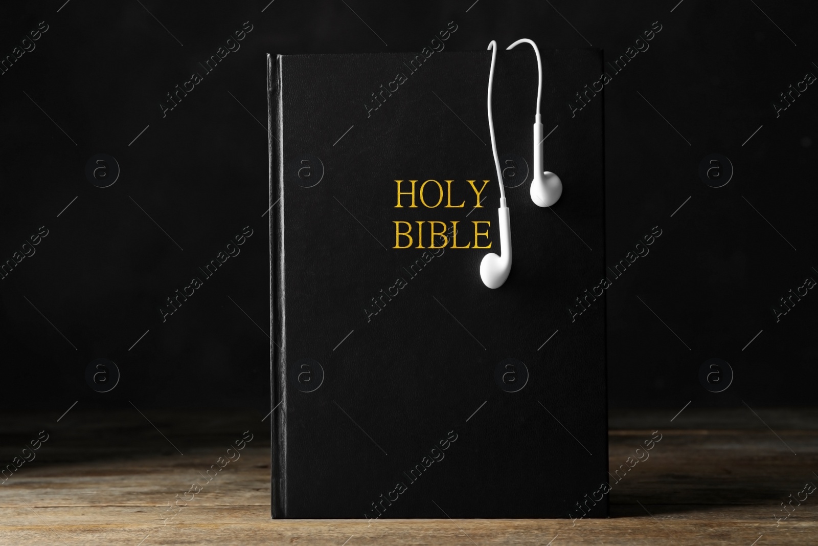 Photo of Bible and earphones on wooden table. Religious audiobook