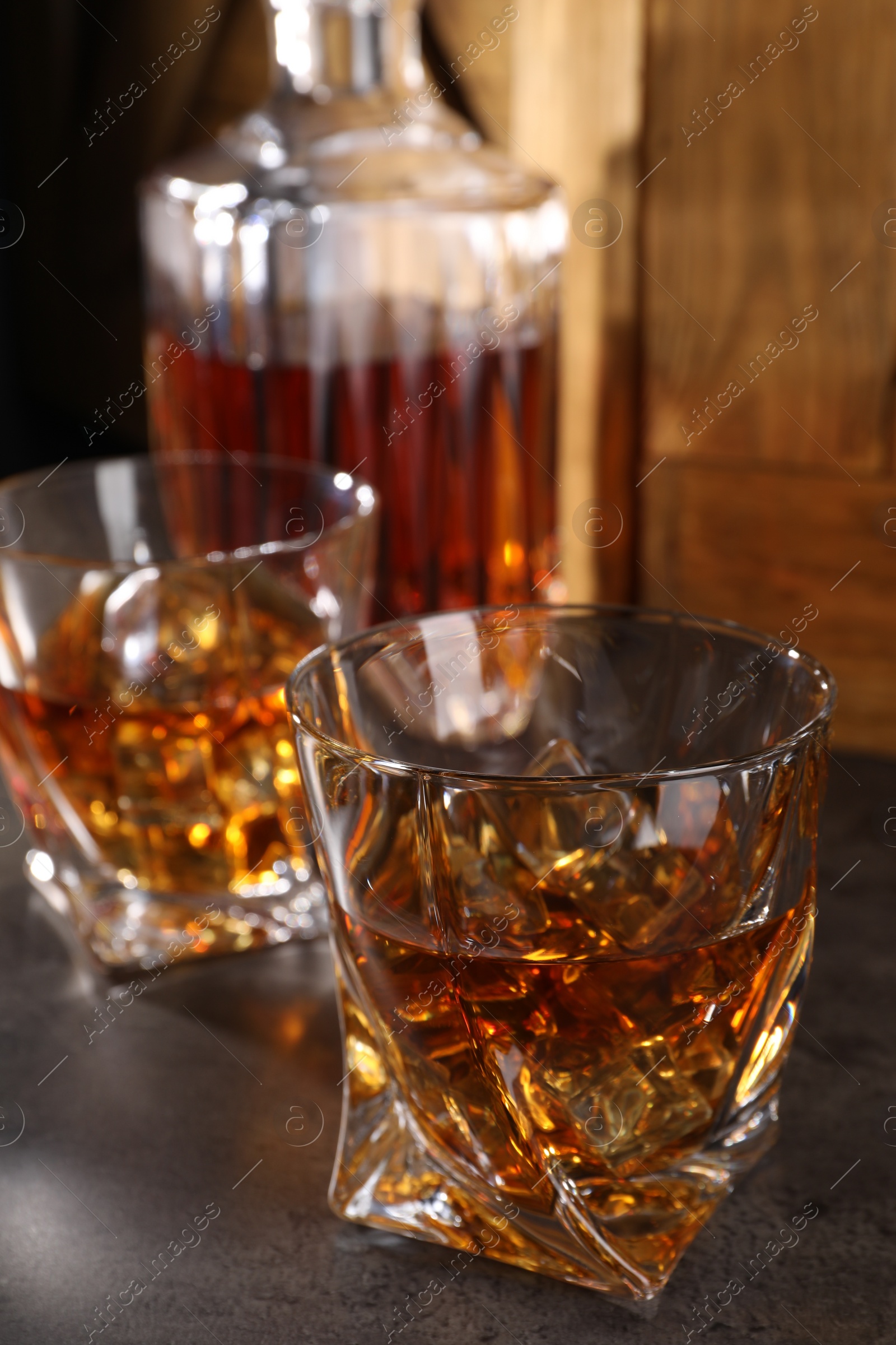 Photo of Whiskey with ice cubes in glasses and bottle on grey table, closeup