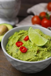 Photo of Bowl of delicious guacamole and ingredients on wooden table, closeup