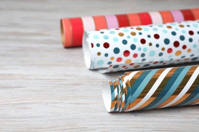 Photo of Different colorful wrapping paper rolls on white wooden table, closeup. Space for text