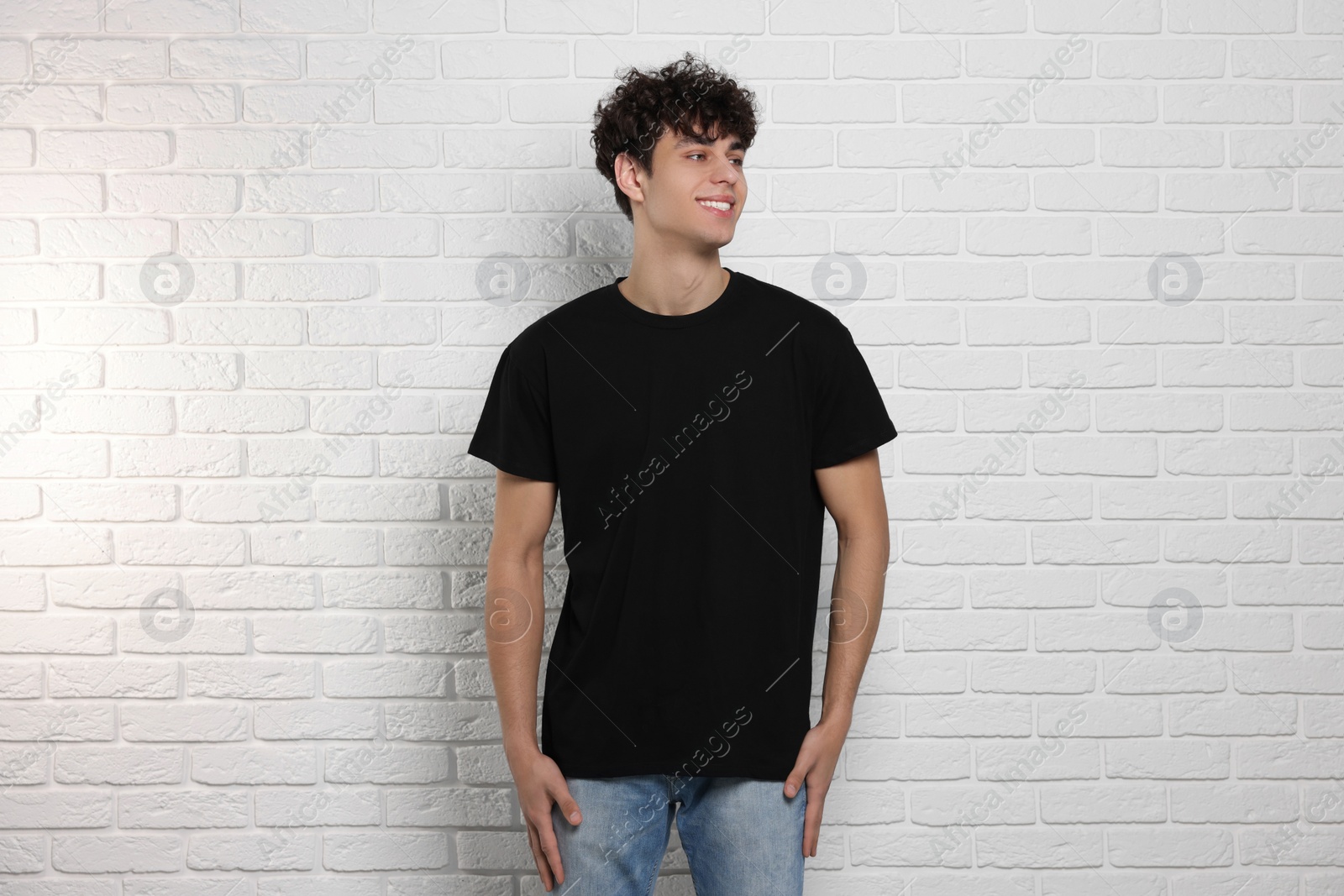 Photo of Man wearing black t-shirt near white brick wall. Mockup for design