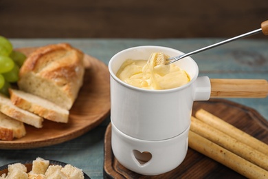 Pot of tasty cheese fondue and fork with bread on blue wooden table