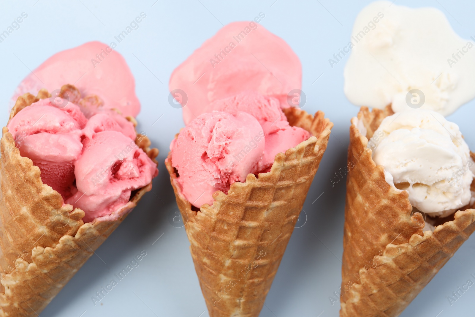 Photo of Melted ice cream in wafer cones on light blue background, flat lay