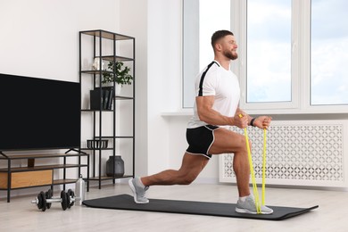 Photo of Athletic man doing exercise with elastic resistance band on mat at home