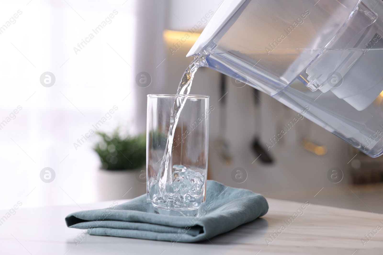 Photo of Pouring water from filter jug into glass in kitchen, closeup