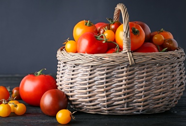 Composition with fresh ripe tomatoes and wicker basket on wooden table