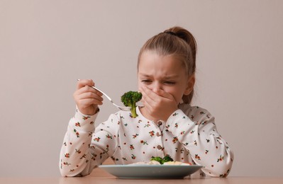 Photo of Cute little girl covering mouth and refusing to eat her dinner at table on grey background