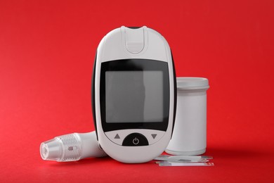 Photo of Digital glucometer, lancet pen and test strips on red background. Diabetes control