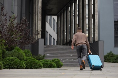 Photo of Being late. Man with suitcase running towards building outdoors, space for text