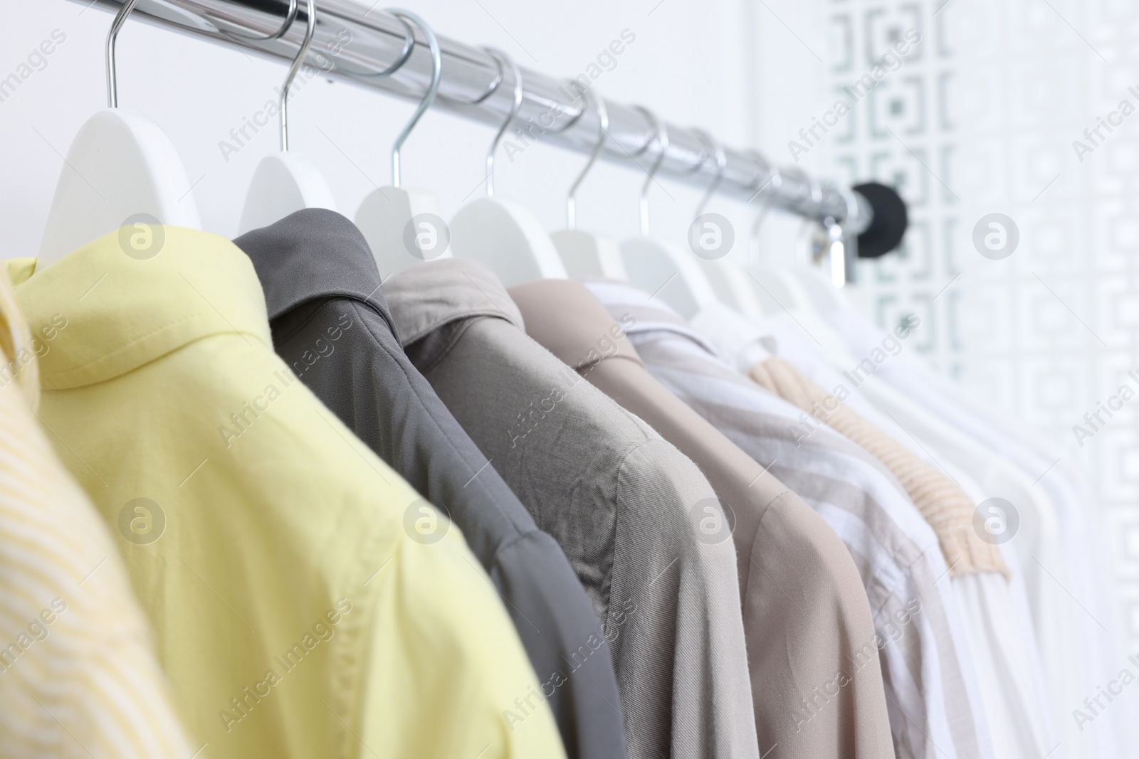 Photo of Rack with different stylish shirts near white wall, closeup. Organizing clothes