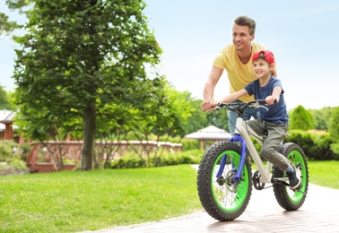 Photo of Dad teaching son to ride bicycle outdoors