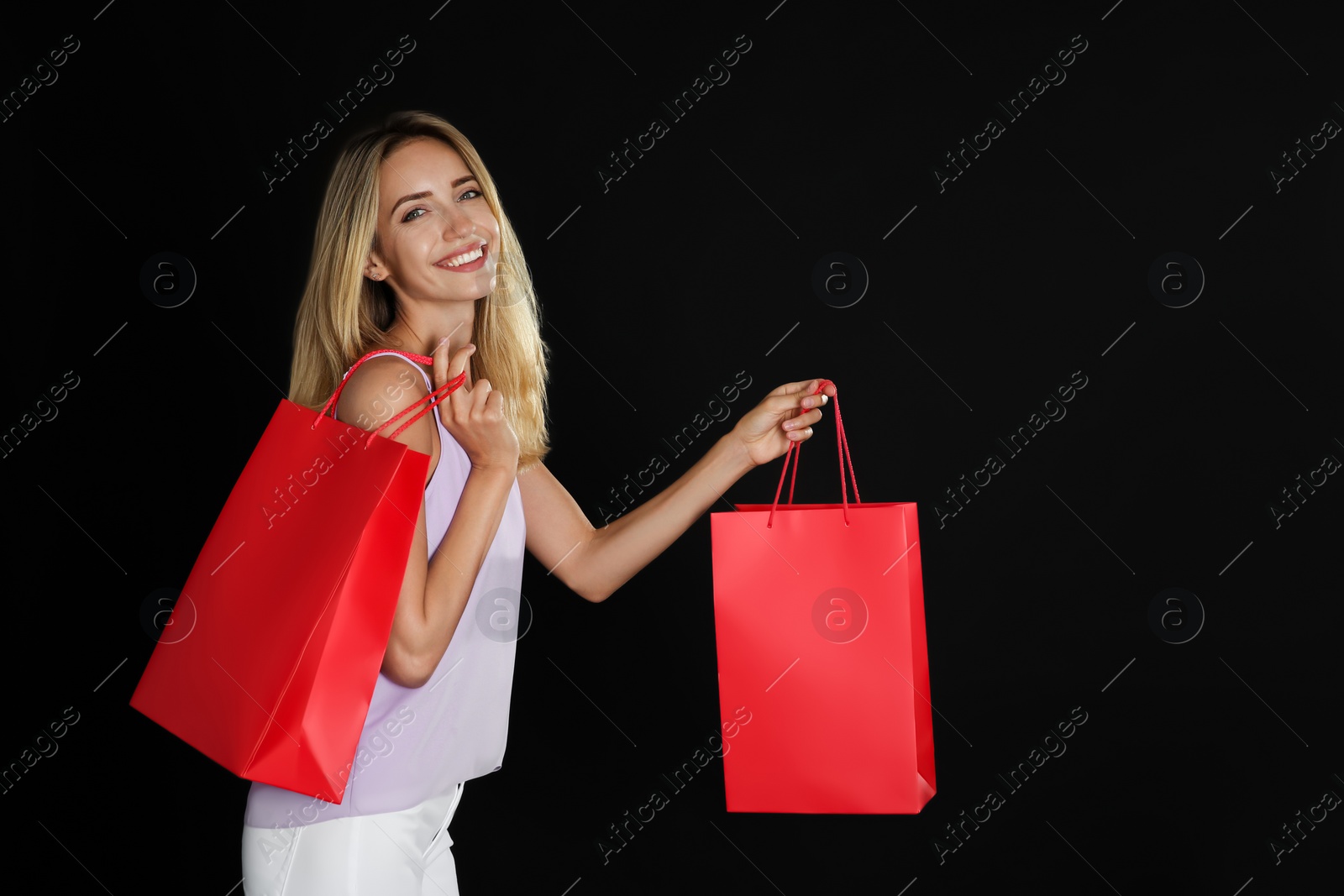 Photo of Happy young woman with shopping bags on dark background. Black Friday Sale