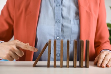 Woman causing chain reaction by pushing domino tile at table, closeup