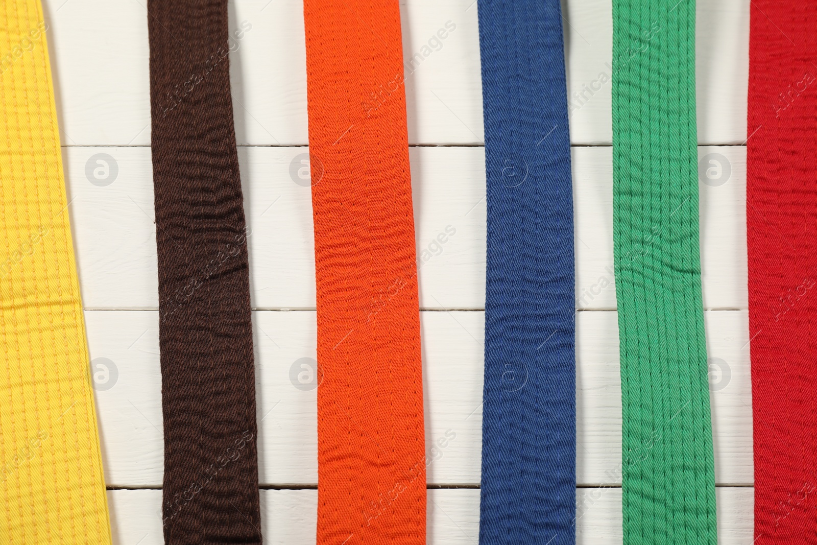 Photo of Colorful karate belts on wooden background, flat lay