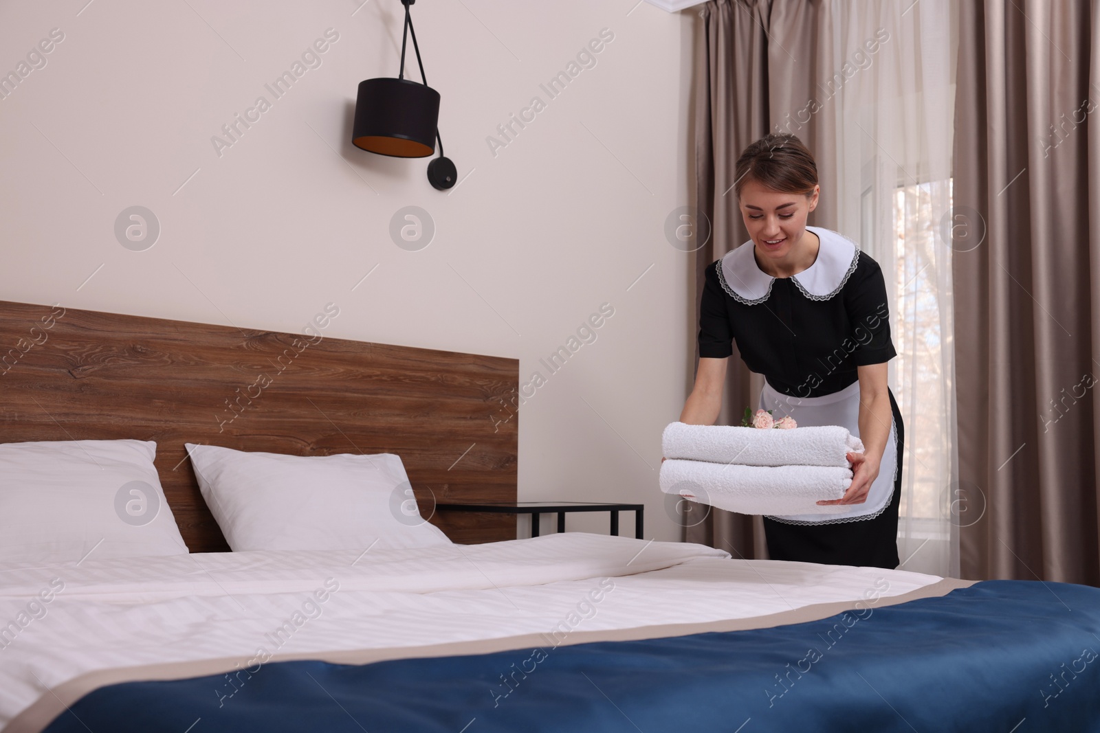 Photo of Beautiful chambermaid putting fresh towels on bed in hotel room