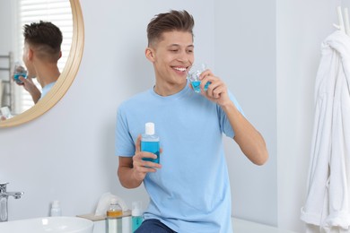 Young man using mouthwash in bathroom. Oral hygiene