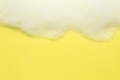 Photo of Fluffy bath foam on yellow background, top view. Space for text