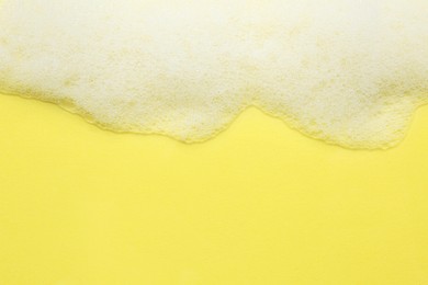 Fluffy bath foam on yellow background, top view. Space for text