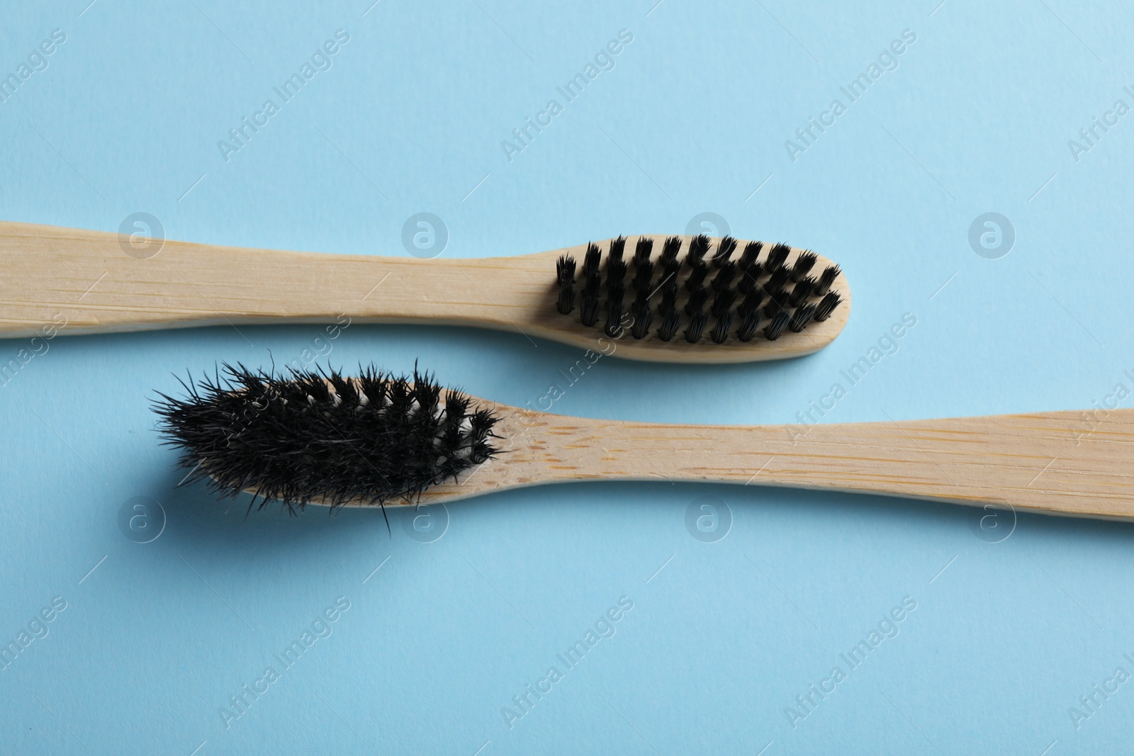 Photo of Two bamboo toothbrushes on light blue background, flat lay