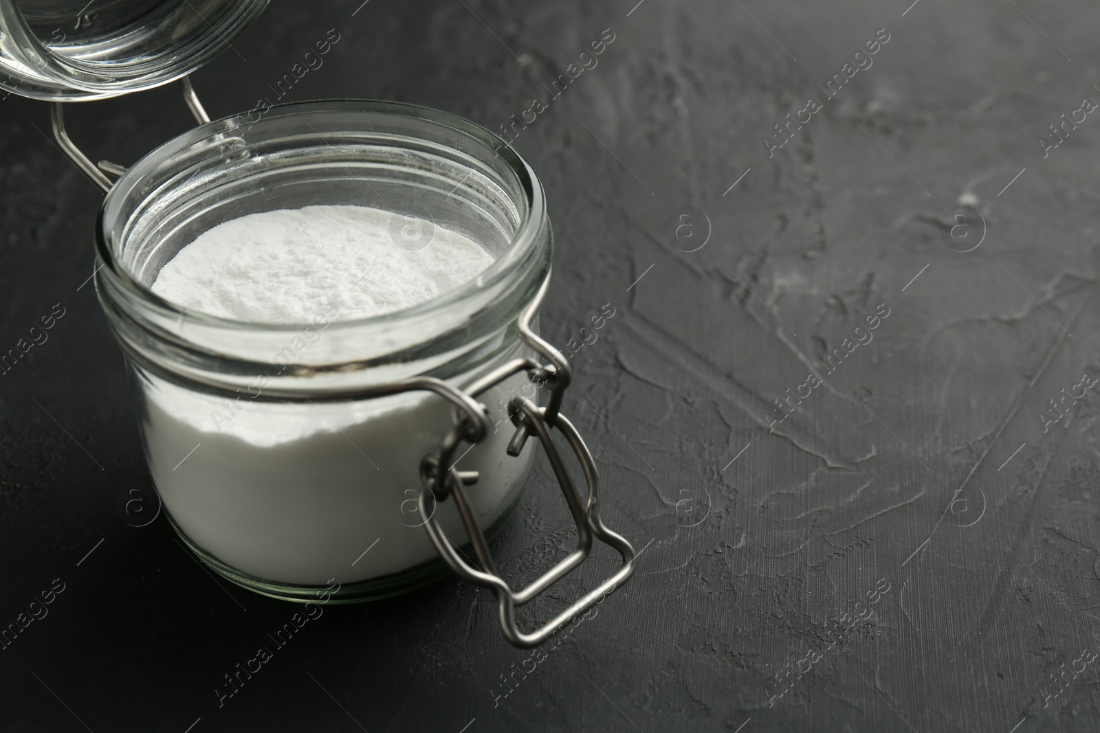 Photo of Baking powder in jar on black textured table, space for text