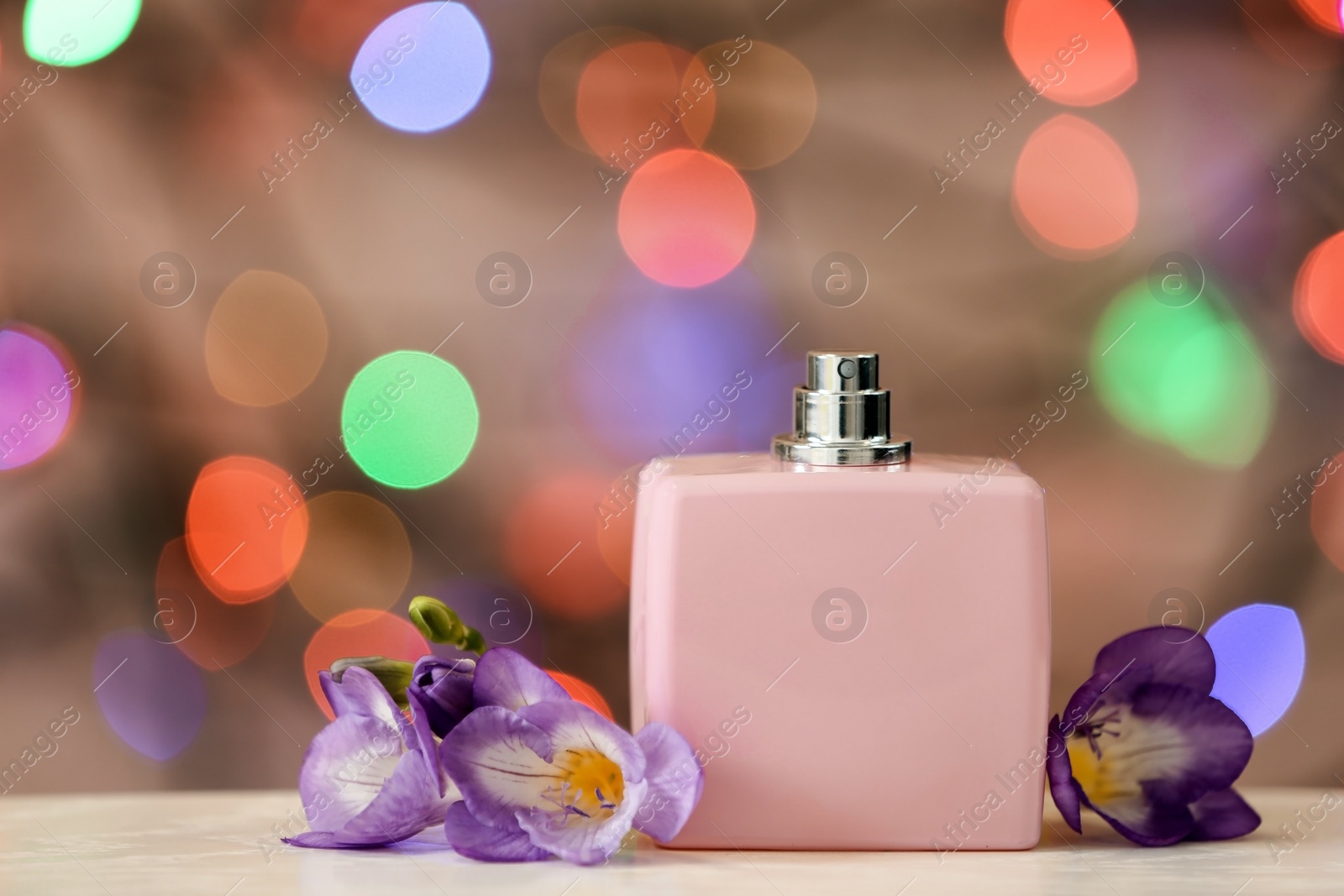 Photo of Bottle of perfume and flowers on table against blurred lights. Space for text